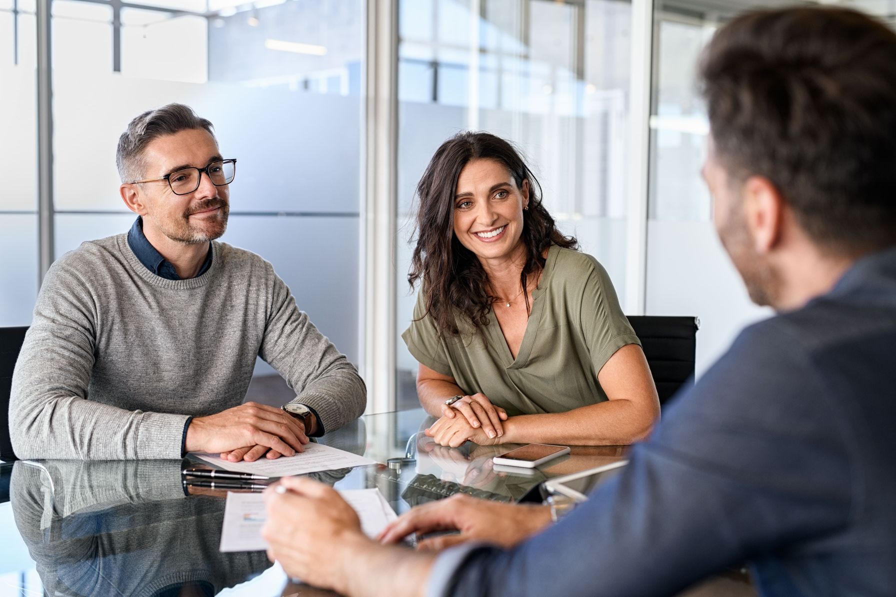 A smiling couple discussing financial planning with an advisor in a modern office.